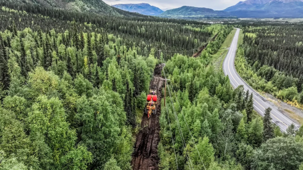 A cable plowing machine works near a rural roadside in Alaska.