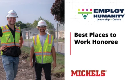 Two young men wearing PPE smile while on a project site.