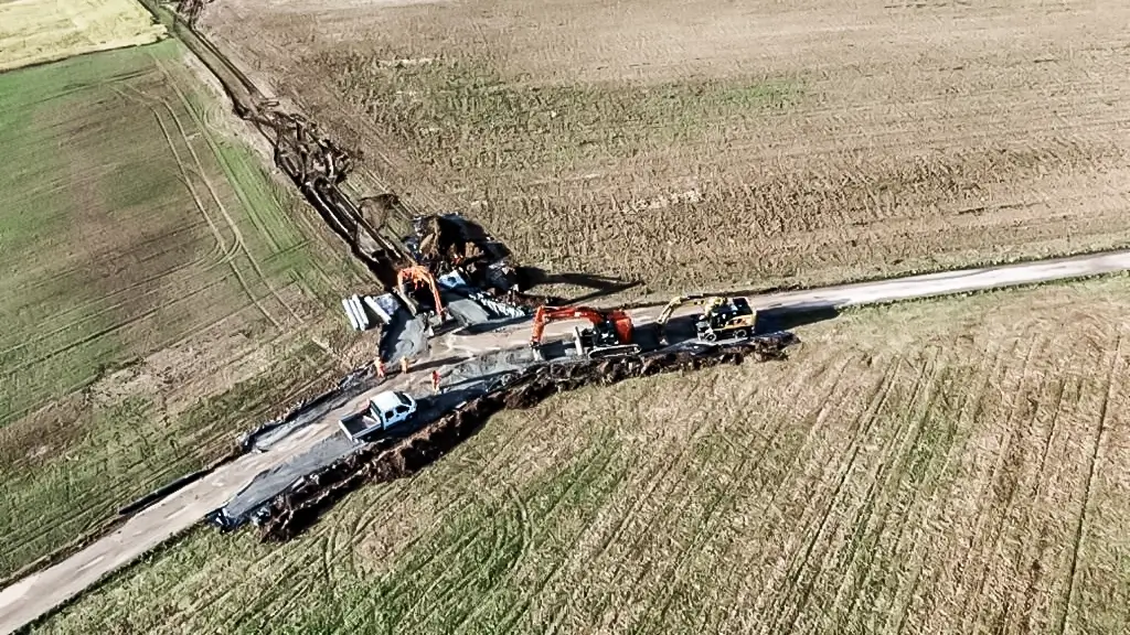 Excavators operate near a rural roadside.