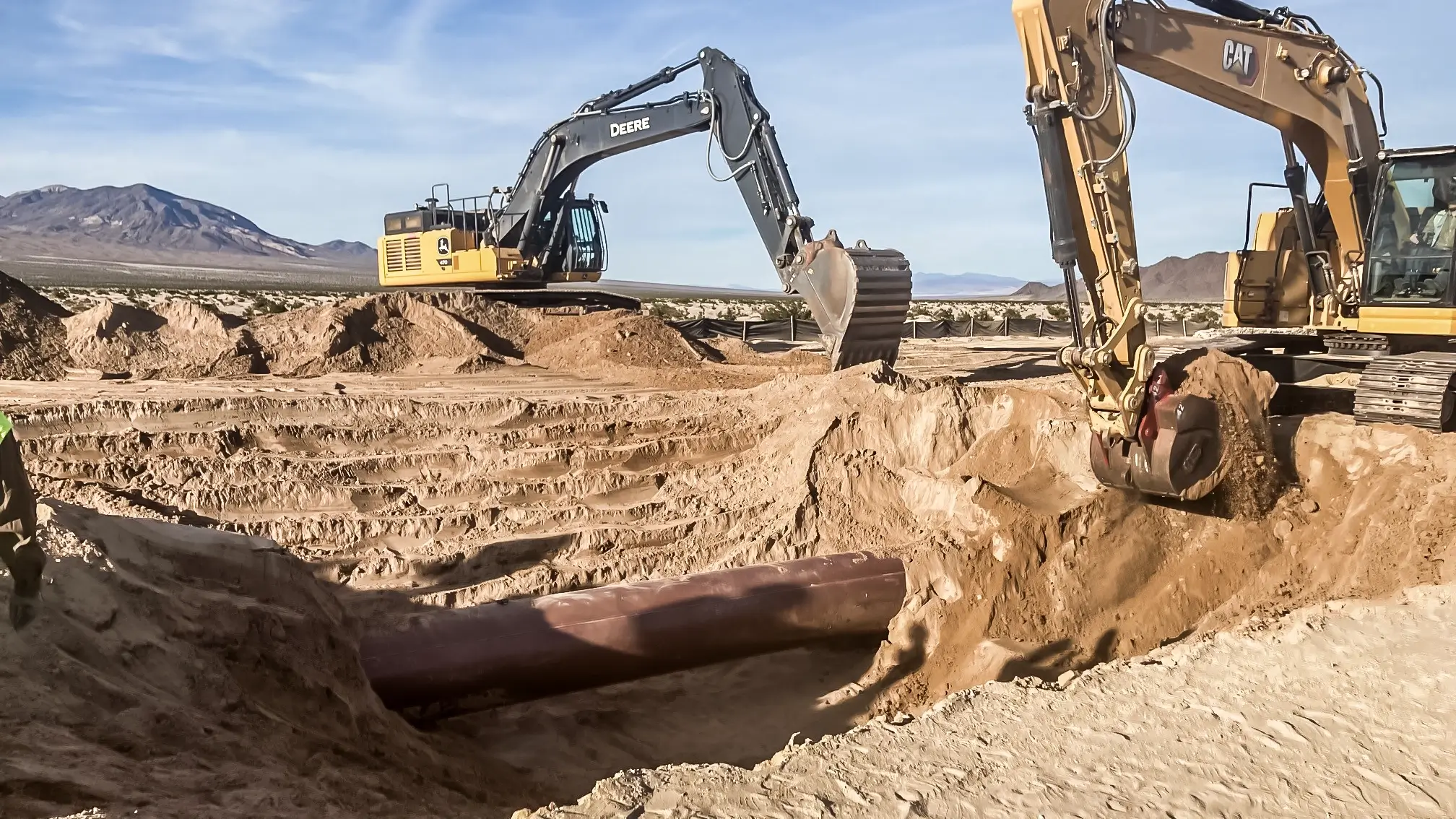 Several excavators dig out an old pipeline in a desert area.