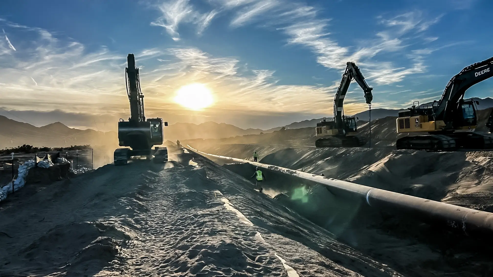 Several excavators operate near a pipeline at sunrise