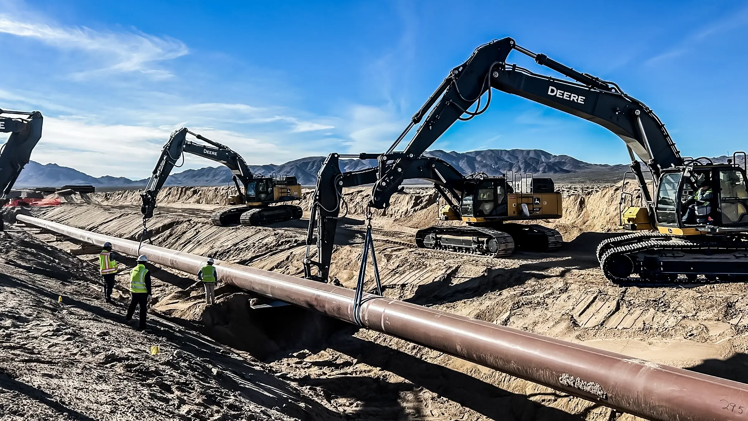 Several excavators work to place a pipeline in its proper position.