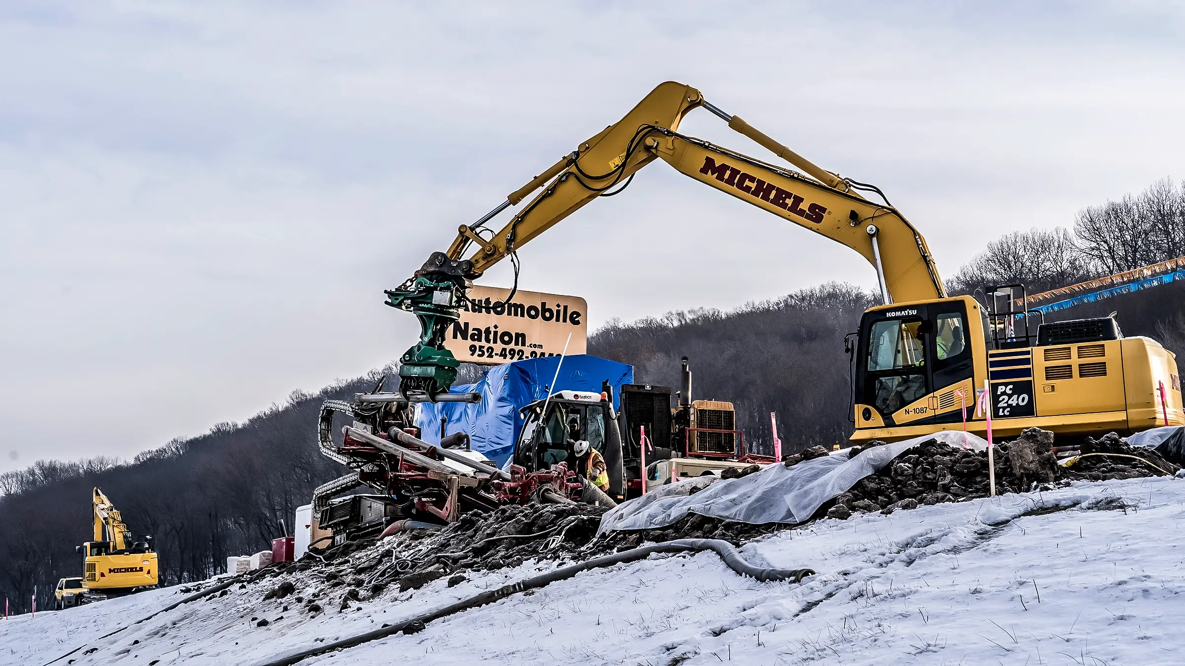 An excavator and HDD rig work simultaneously on top of a snowy hilltop.