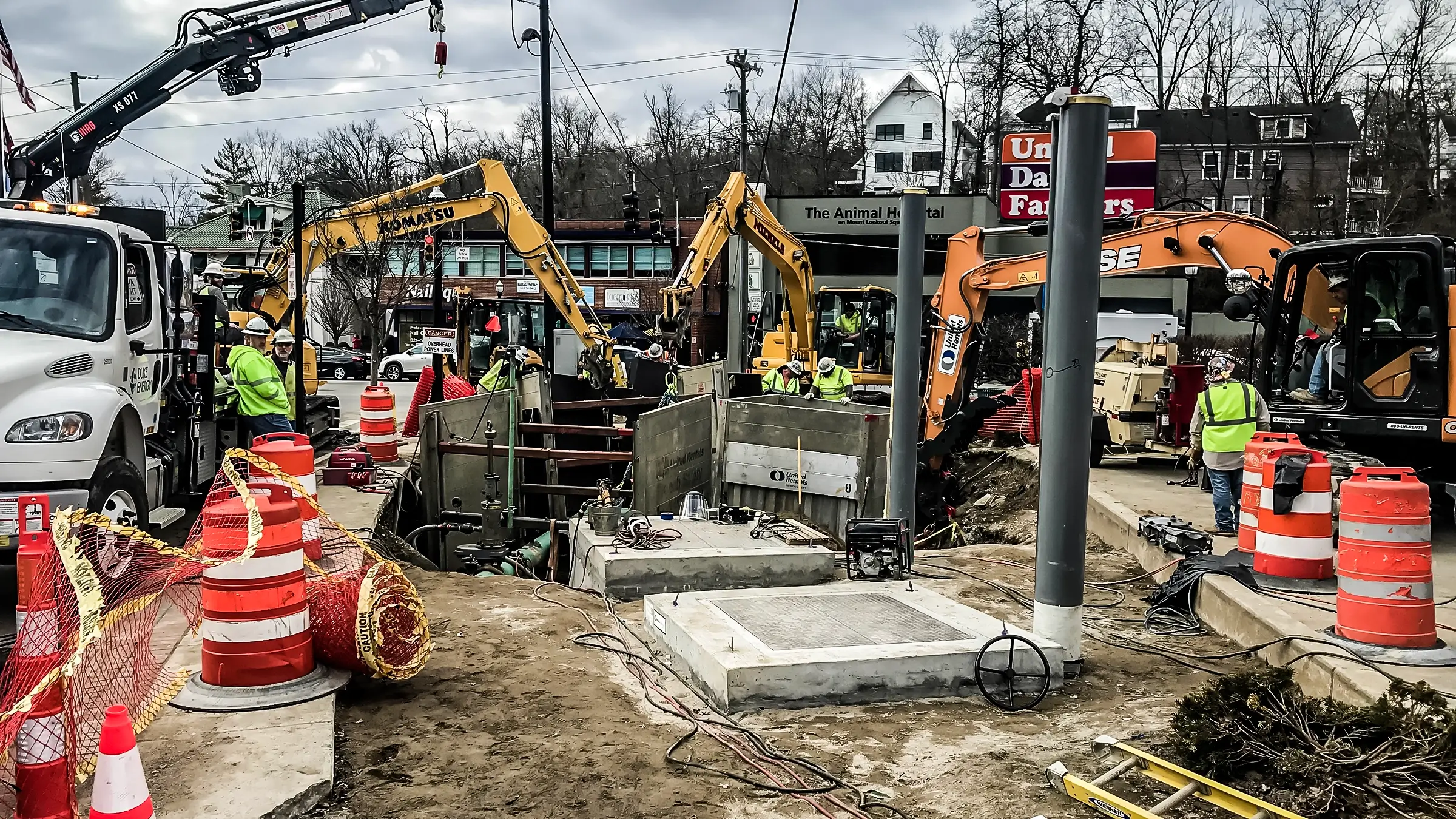 Several small excavators and crew members operate in a busy downtown jobsite.