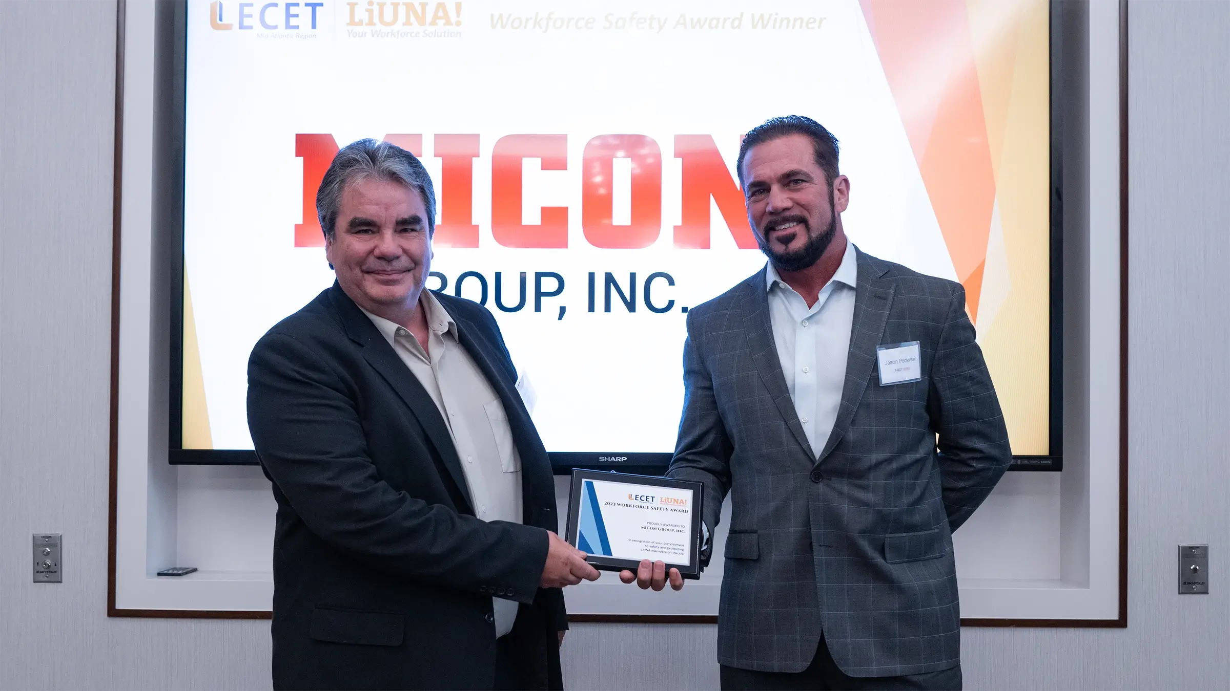 Two men on a stage with one handing award to the other.