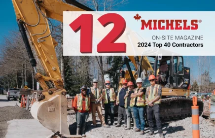 A group of employees stand near an excavator.