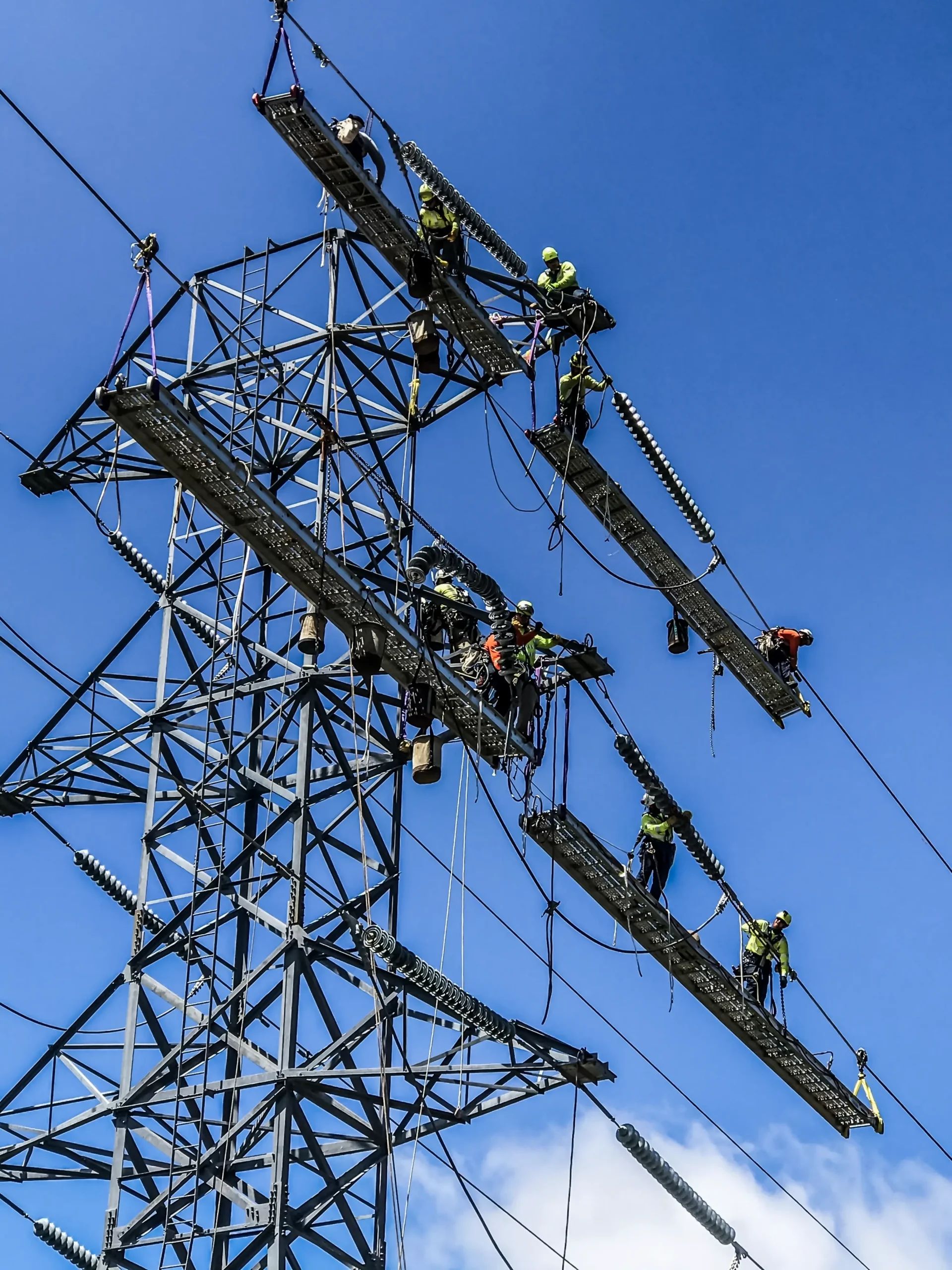 Several linemen work on up high on a large power transmission line segment.