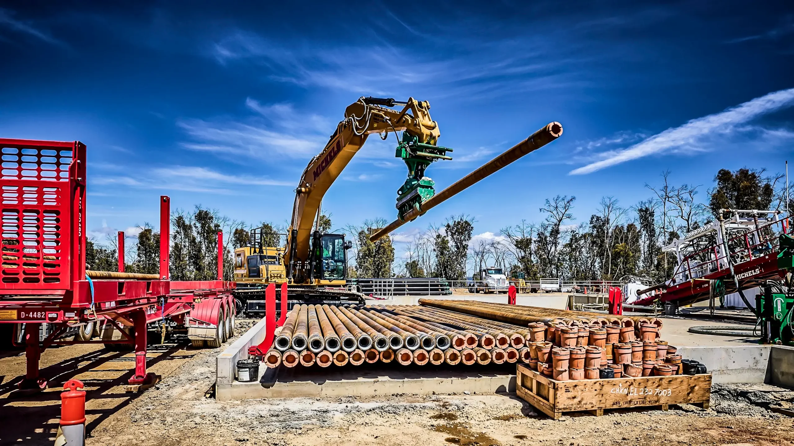 An excavator picking up a piece of HDD pipe to place into HDD rig.