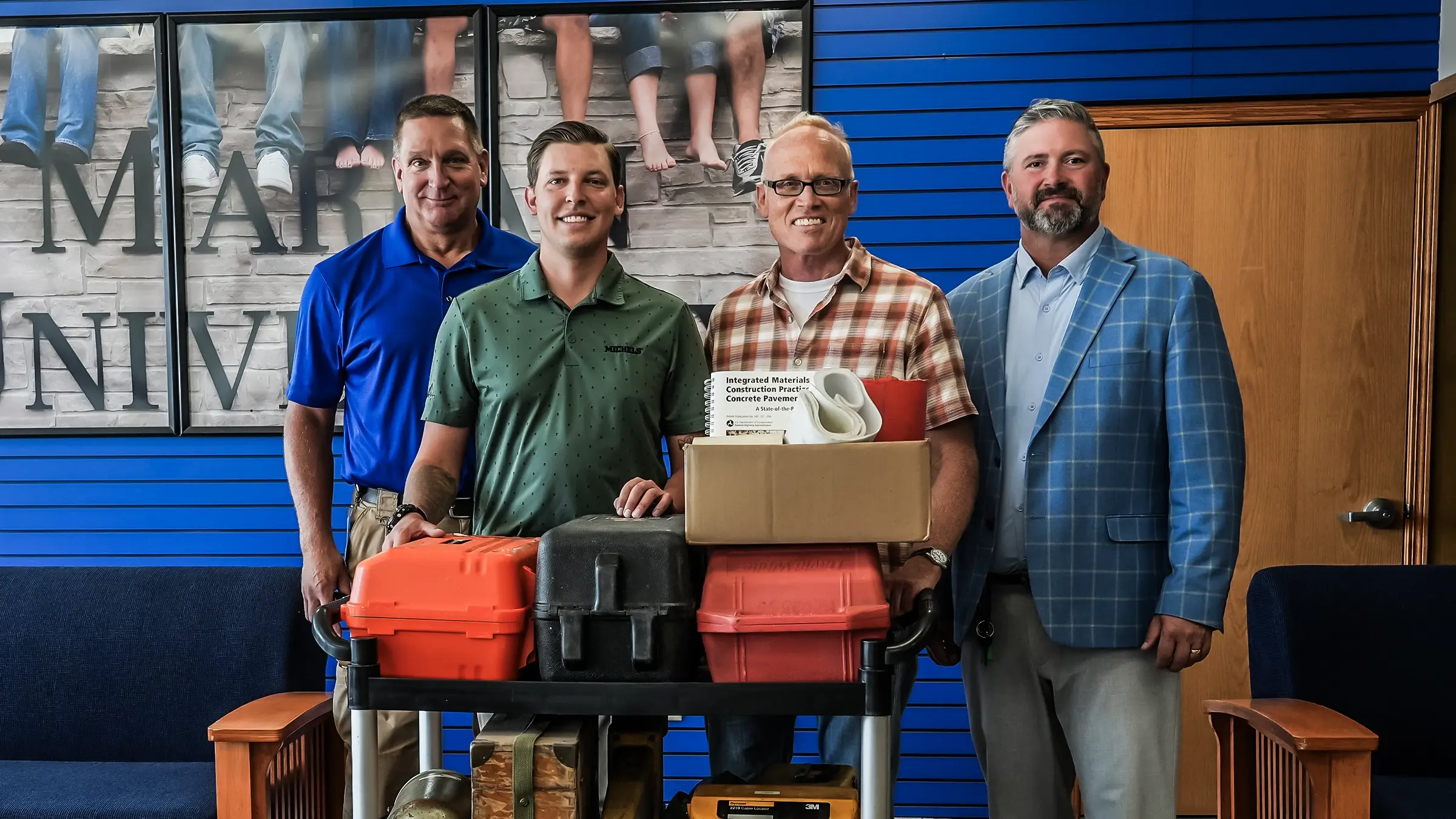 Four men stand near a cart containing donations to Marian University.