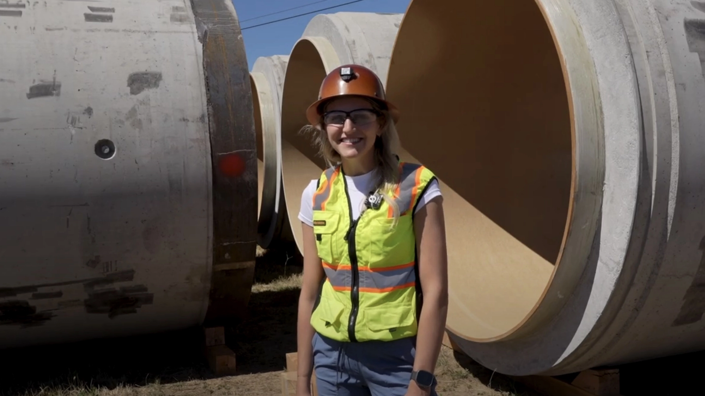 A woman stands near large diameter tunnel pieces.