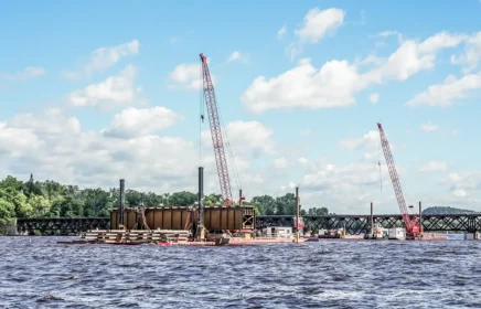 A set of cranes work on barges to move portions of a railroad on a river.