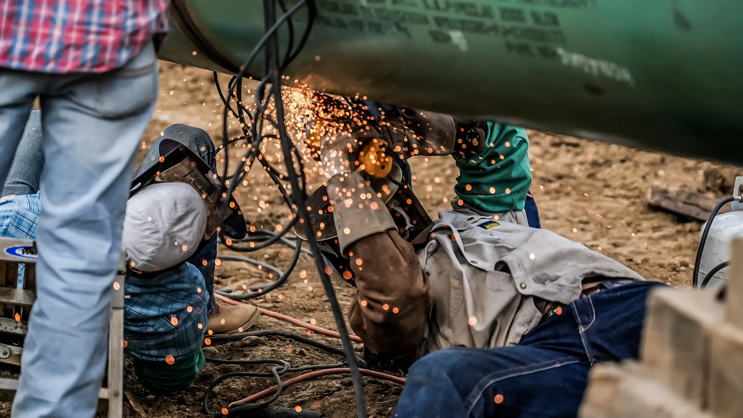 A man wearing a welder mask works on the bottom portion of a large diameter pipe.