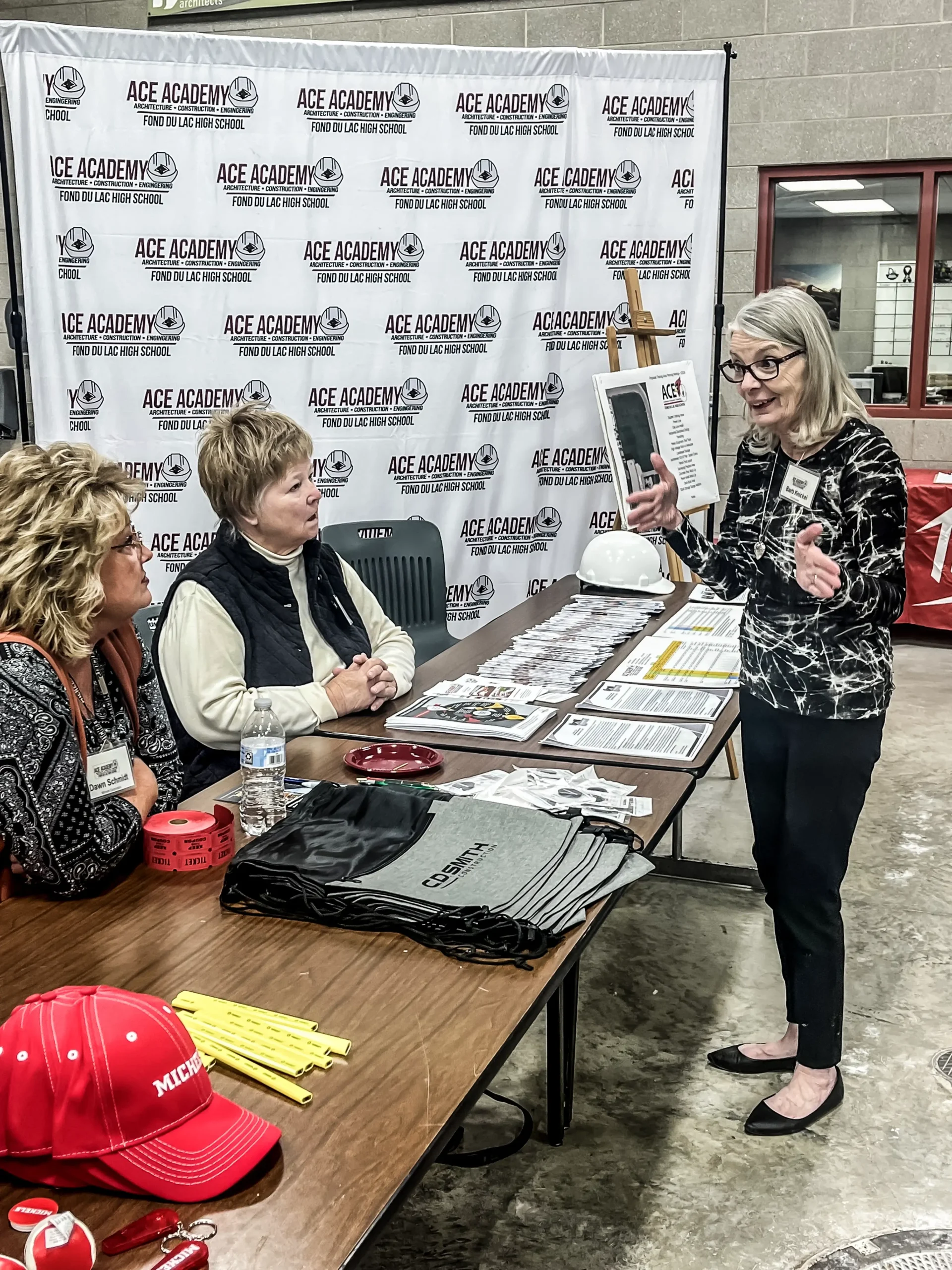 Three women talk at a school booth.