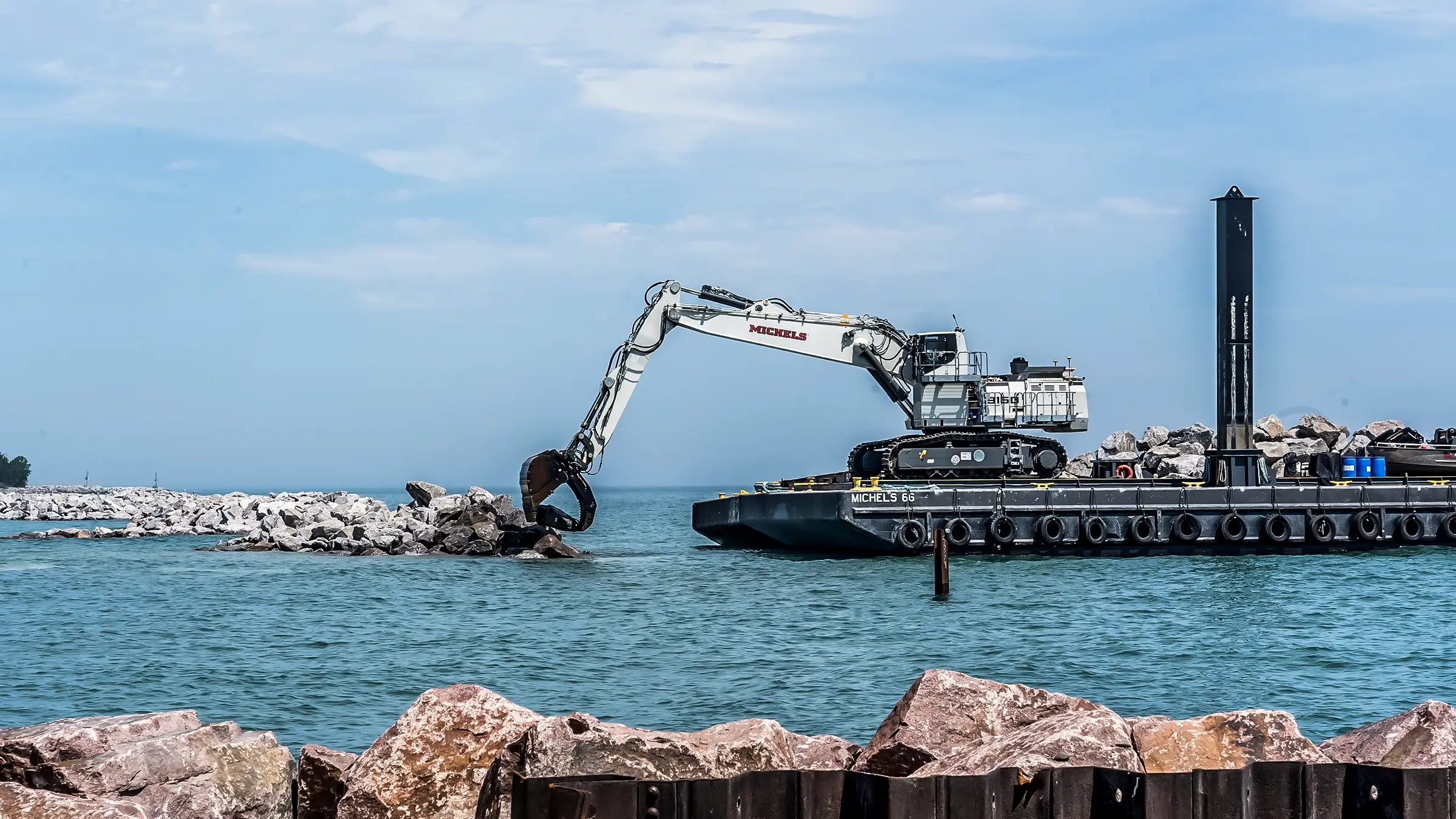 An excavator works on a barge to lift shoreline rocks.