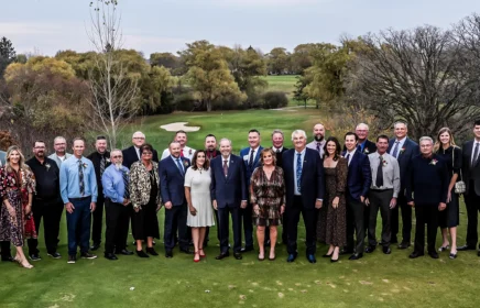 Large group of people standing on a golf tee box.