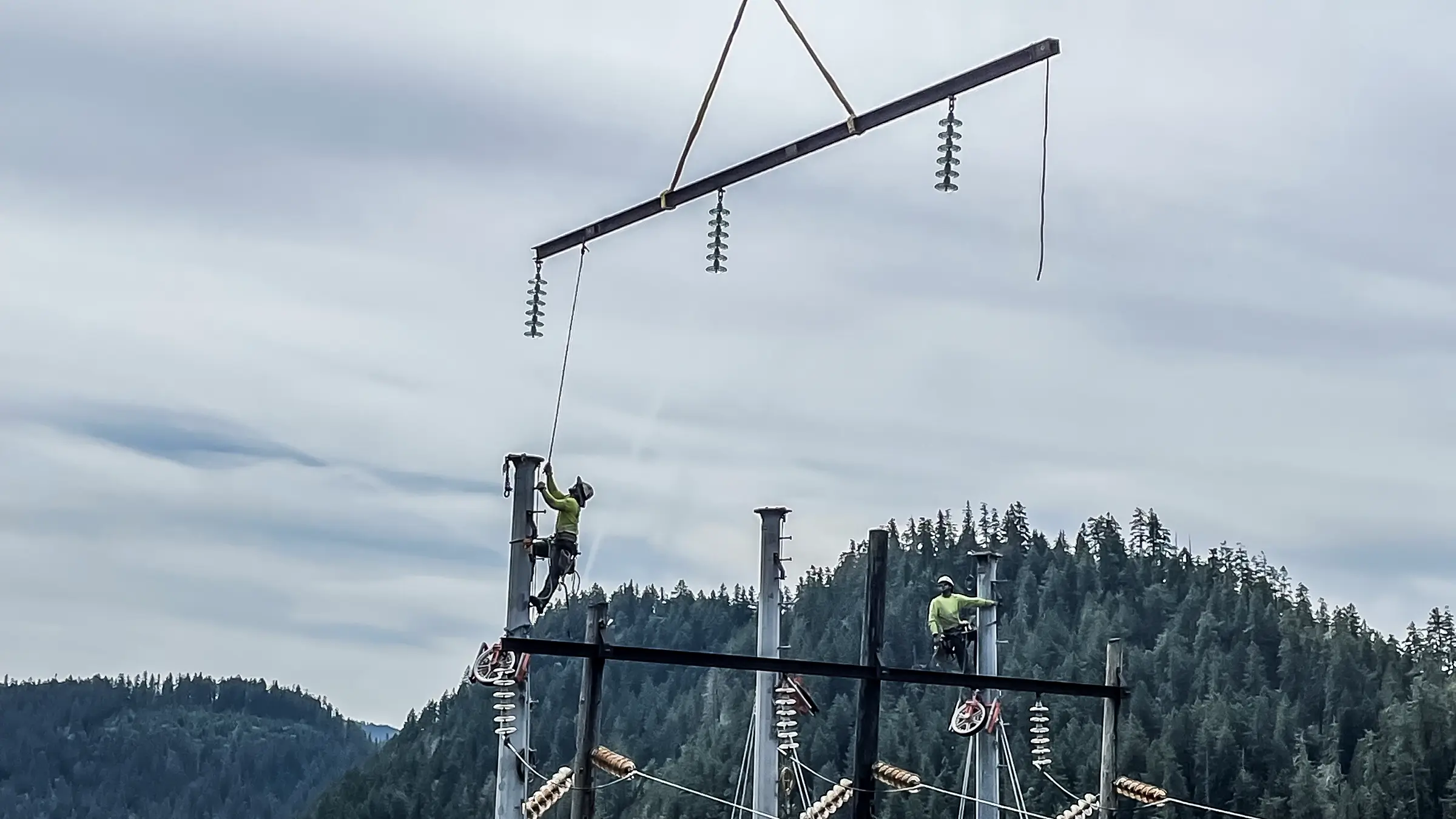 Crew members on top of a transmission tower assist in putting a piece of tower in its place.