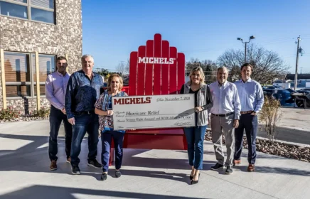 Michels Family member stand outside the Michels Headquarters with a large check.