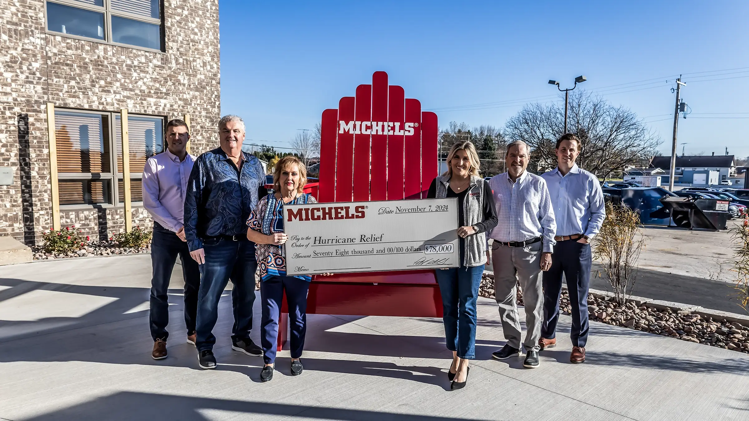 Michels Family member stand outside the Michels Headquarters with a large check.