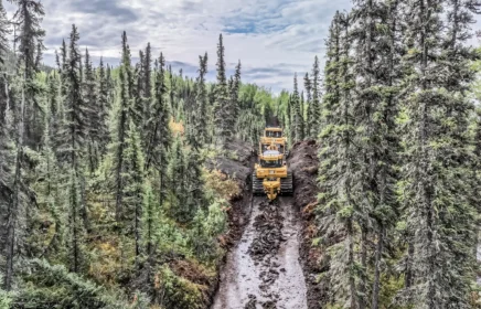 A utility plow makes its way through thick forest of Alaska.