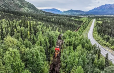 A cable plow going through a forest in Alaska with mountains in view.