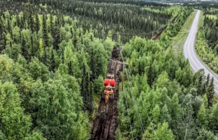 A cable plow going through a forest in Alaska with mountains in view.